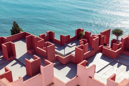 View from above of La Muralla Roja by Ricardo Bofill in Calp, Spain - the rooftop of the building featuring red and pink walls of varying heights beside the sea