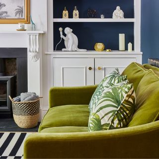 Green velvet sofa in a living room with built-in bookshelves and blue walls