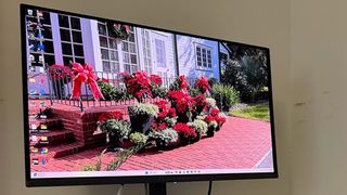 A computer monitor displays a bright desktop wallpaper of a white house, red brick steps and path, and vivid flowers in a sunny garden.