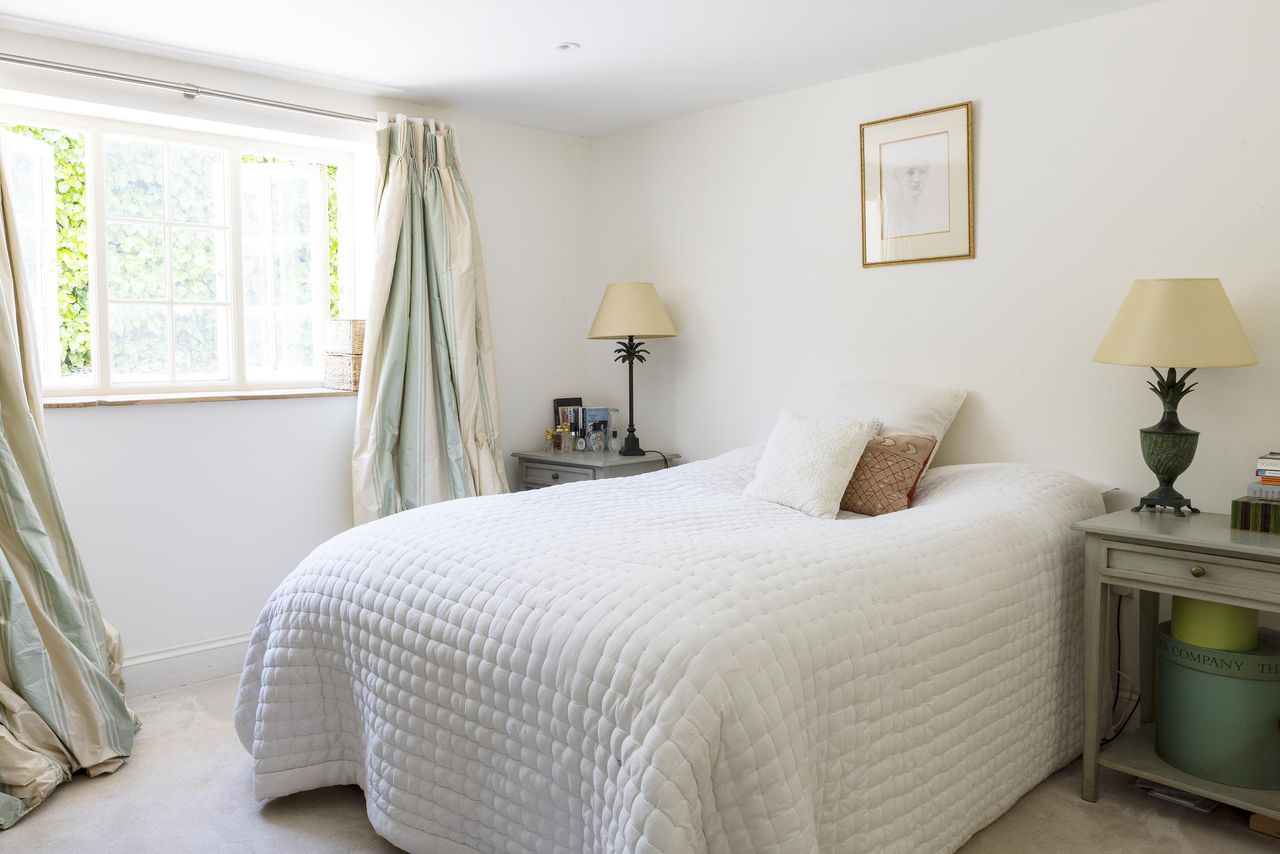 A bedroom inside Mount Farm with a bed with white bedding and teal curtains