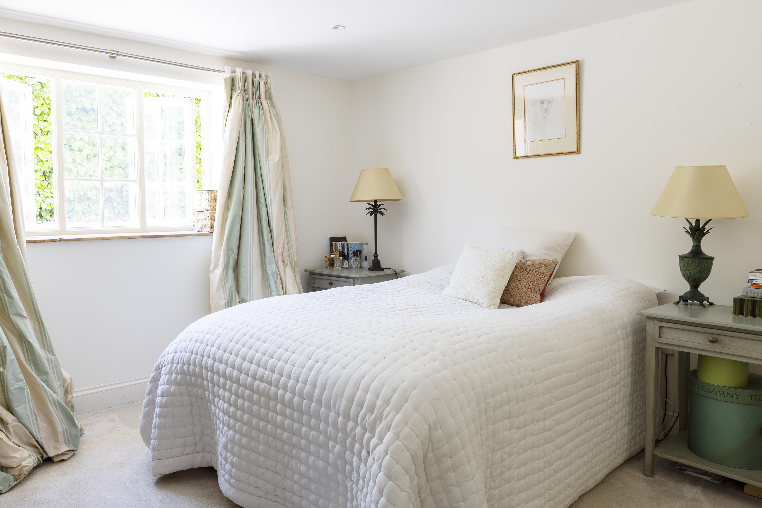 A bedroom inside Mount Farm with a bed with white bedding and teal curtains
