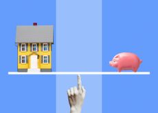 Yellow miniature model house and pink ceramic piggy bank on white line balanced on woman's finger
