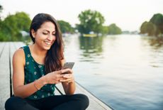 Woman texting on her phone, sitting in front of a lake
