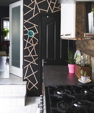 Kitchen with black walls and woodwork, geometric copper lines and pale grey flooring. Claire and Ivan Johnson's redecorated four bedroom Victorian terraced house in Kettering, Northamptonshire.