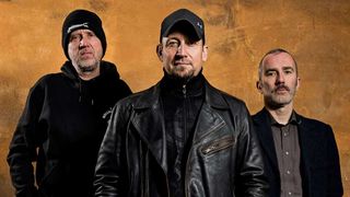 Volbeat standing in front of a brown wall, smiling