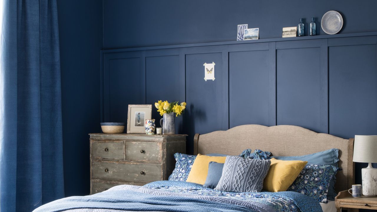 A blue-painted bedroom with wall panelling and matching curtains