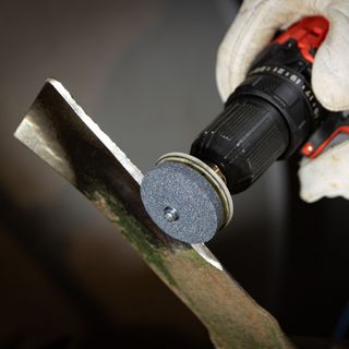 Someone using a tool attachment to sharpen lawn mower blades