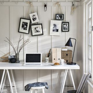 white wall with pictures hanging and white desk and black lamp