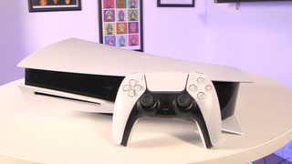 En Playstation 5 ligger på ett vitt bord med en matchande spelkontroller som står lutad mot sidan av spelkonsolen.