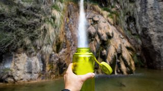 A hiker filling bottle of water from waterfall