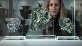 Close ups of the Antikythera mechanism with a womans face peering in from behind.