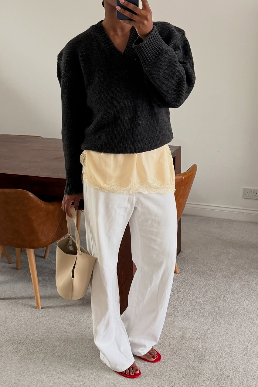 a woman wearing a black sweater, yellow lace-trim top, and white pants