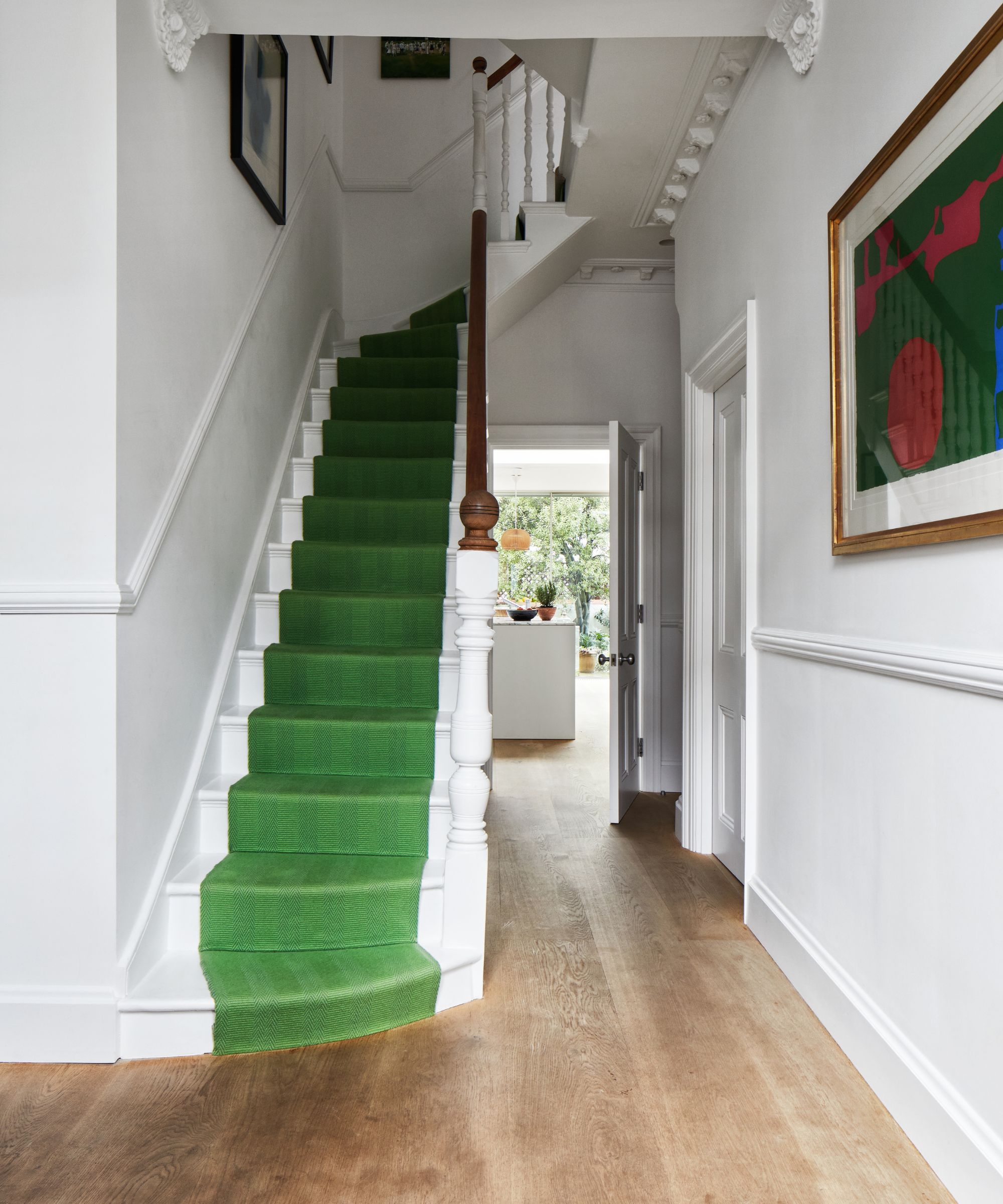 A white entryway with white stairs with a green stair runner, wooden flooring and white walls.
