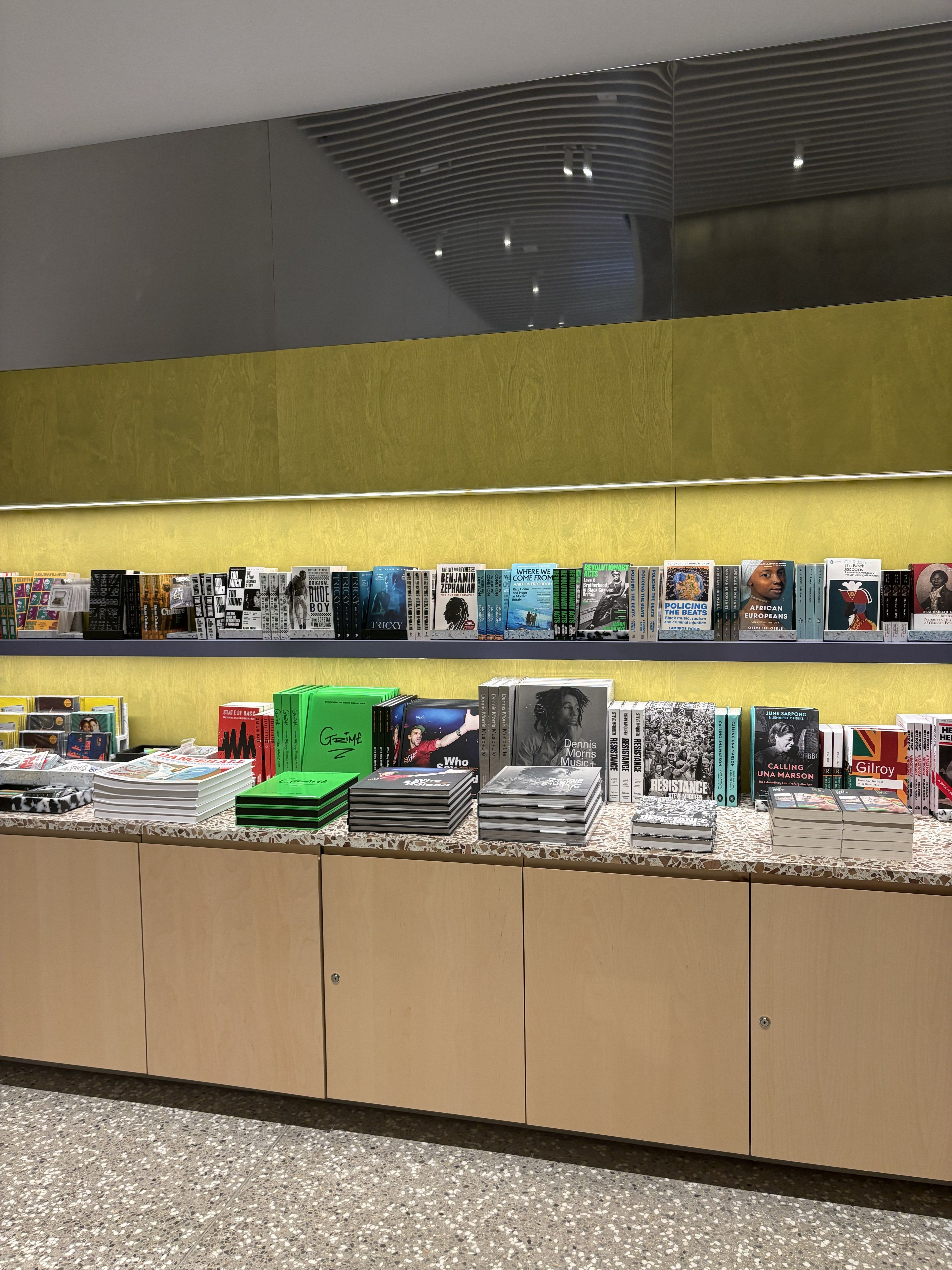 The interior of a museum, featuring a curated book shelf and a towering, pyramidal installation of multiple screens placed atop each other.