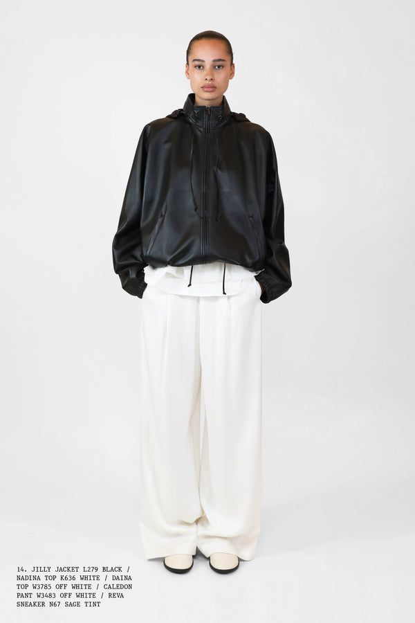 Woman in black technical jacket and white pants.