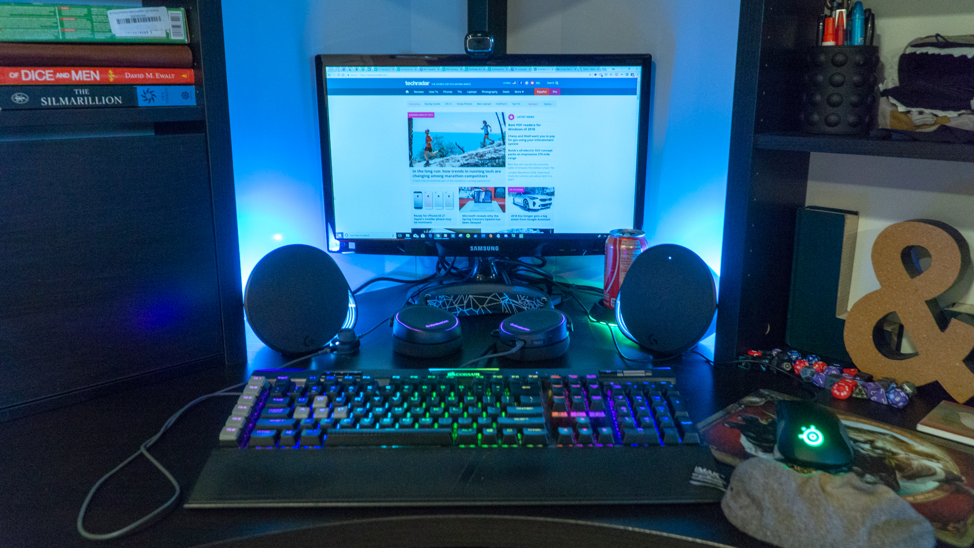 Et par Logitech G560 på et skrivebord ved siden av et gaming-oppsett med tastatur og skjerm