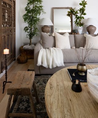A living room with a gery sofa and white throw blanke, and rustic wooden furniture including coffee table and bench