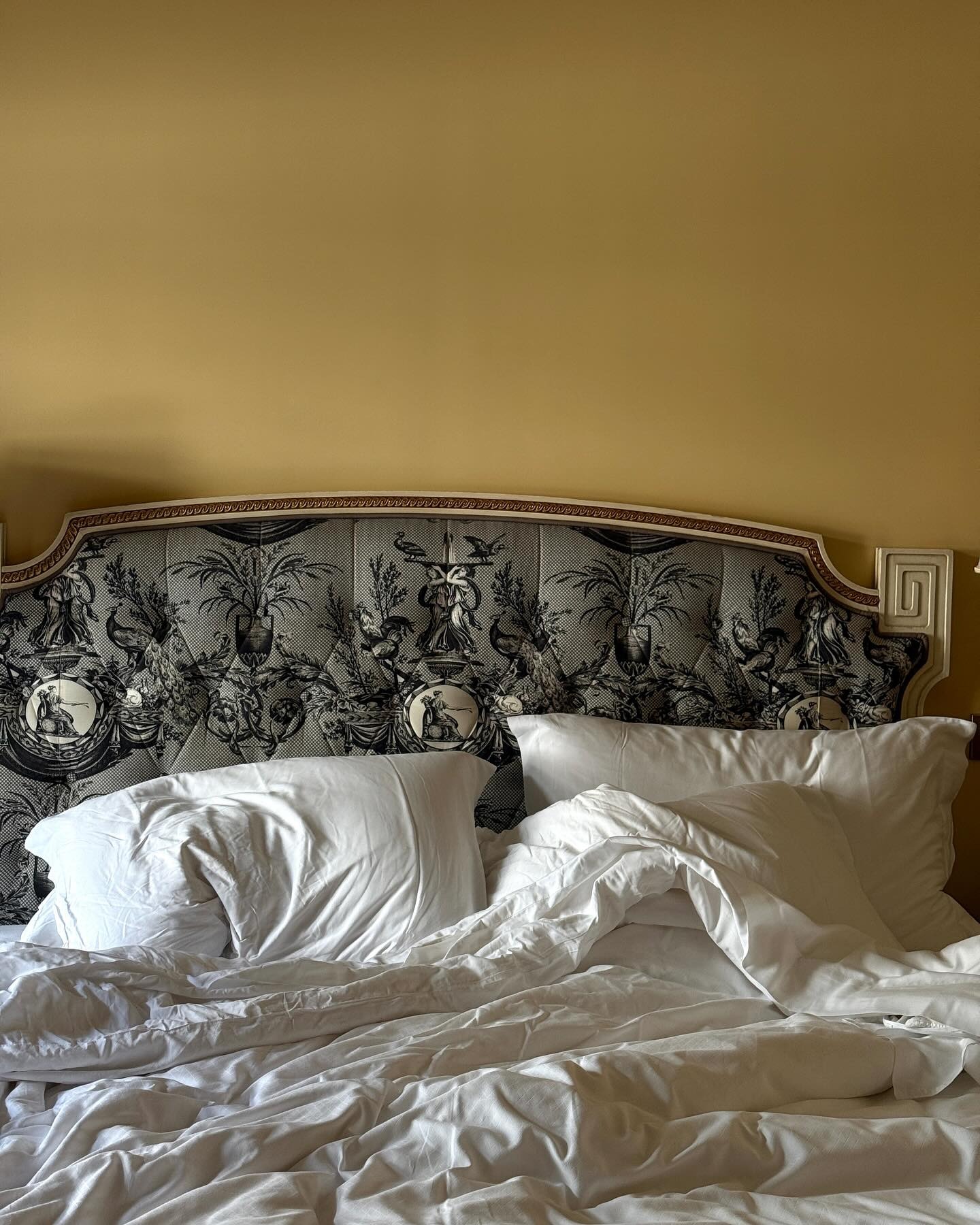 A photo of a cosy, unmade bed with an ornate headboard