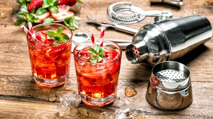 Cocktail-making equipment and two cocktails in tumblers on a wooden worktop