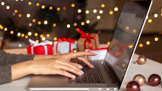 Woman's hands type on MacBook with Christmas tree and holiday decorations all around.
