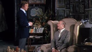 Michael Caine standing next to a sitting Sir Laurence Olivier in Sleuth