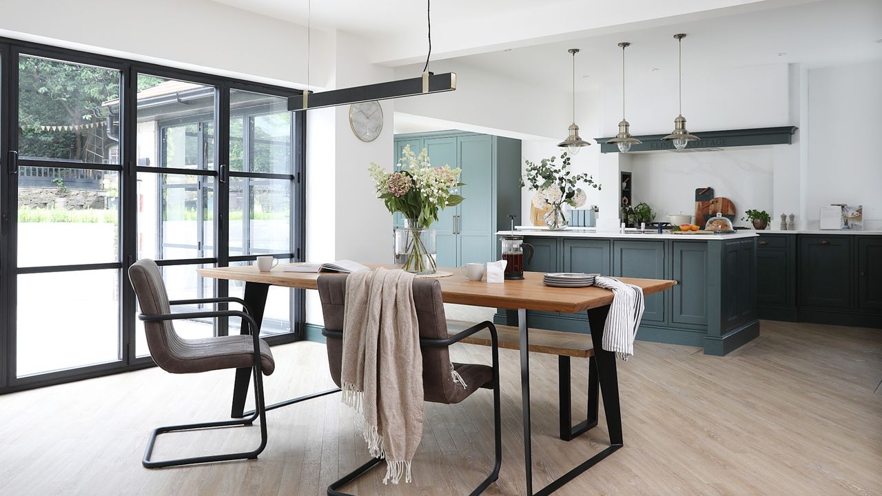 White painted kitchen and dining room with teal kitchen cabinets, wooden dining room, overhead lighting