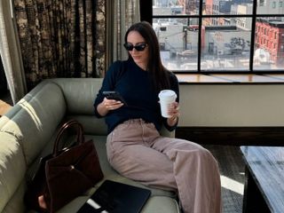 Fashion influencer Liv Perez sitting by a window with the view of New York City wearing a chic fall outfit from Veronica Beard.