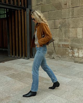 Woman wears brown suede jacket, blue jeans and black boots