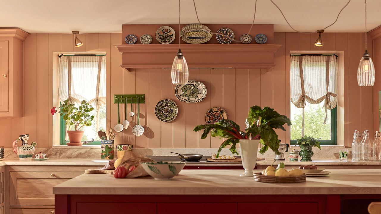 Italian inspired kitchen with pink walls, wooden cabinets and red island with two glass pendants above