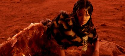 Anna Sawai reclines on red desert rocks in a dark textured top and a shimmering skirt.