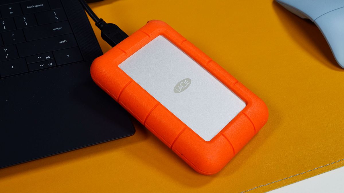 A LaCie Rugged Mini external hard drive on a desk with a laptop