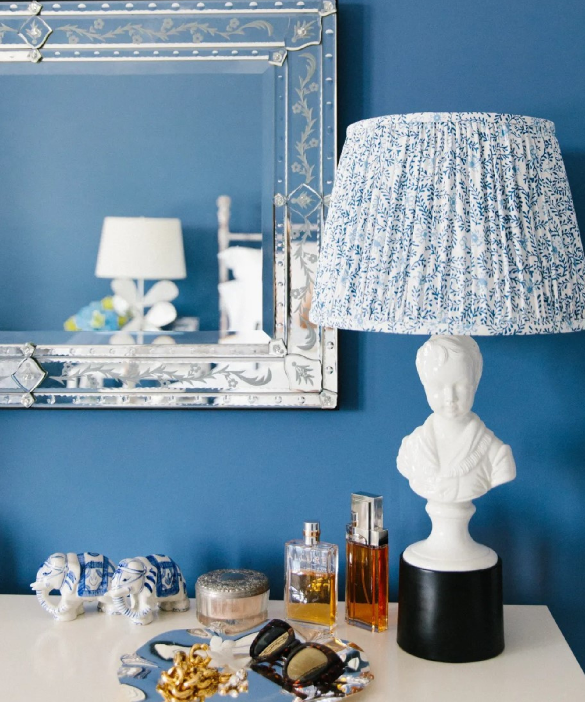 A blue wall with a side table, a white lamp, and antiques.
