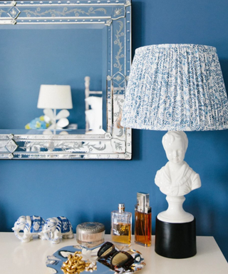 A blue wall with a side table, a white lamp, and antiques.
