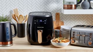 The Russell Hobbs Brooklyn air fryer on a wooden counter surrounded by other appliances, crockery and food