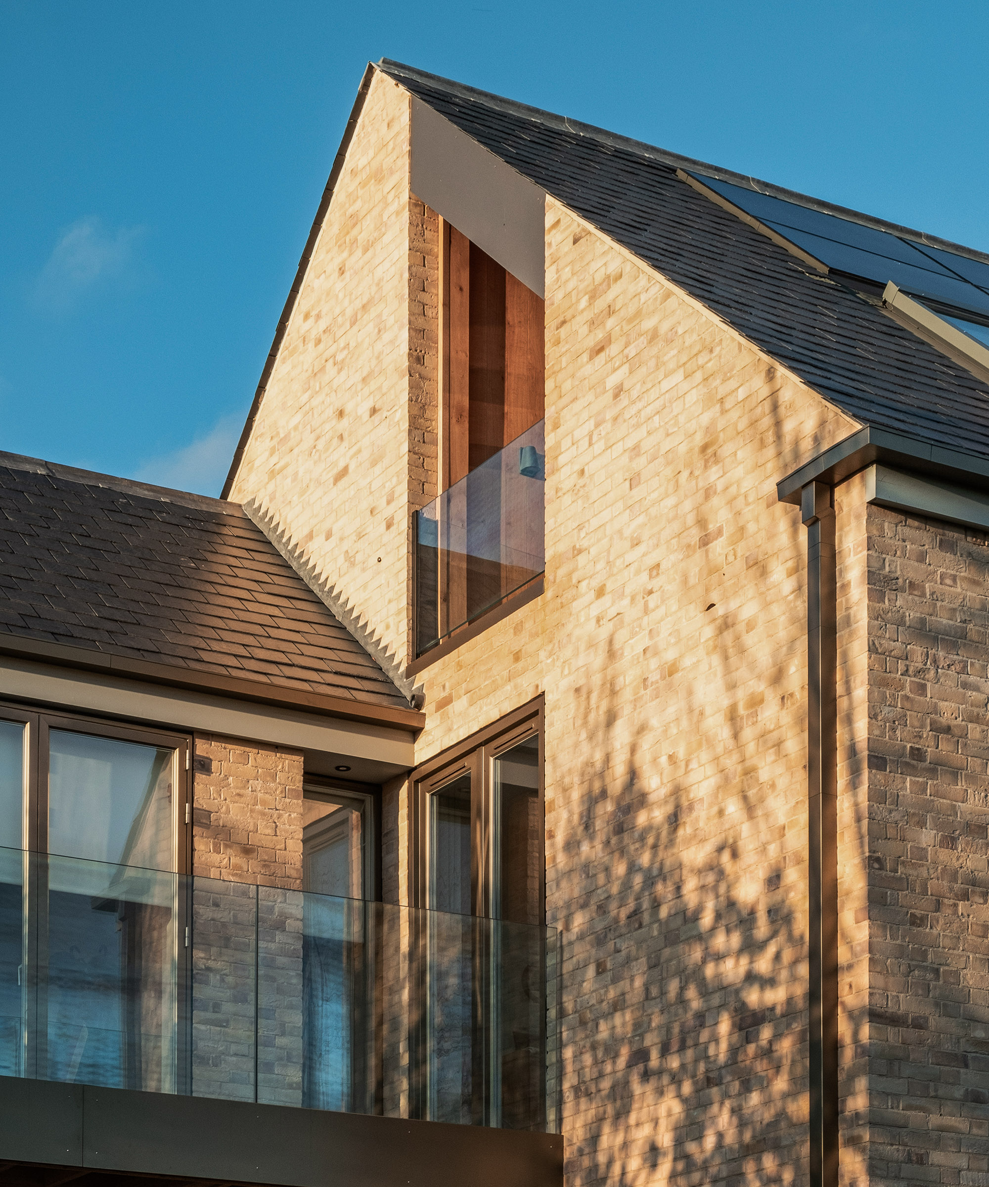 A brick clad self build home with a pitched roof against. aclear blue sky