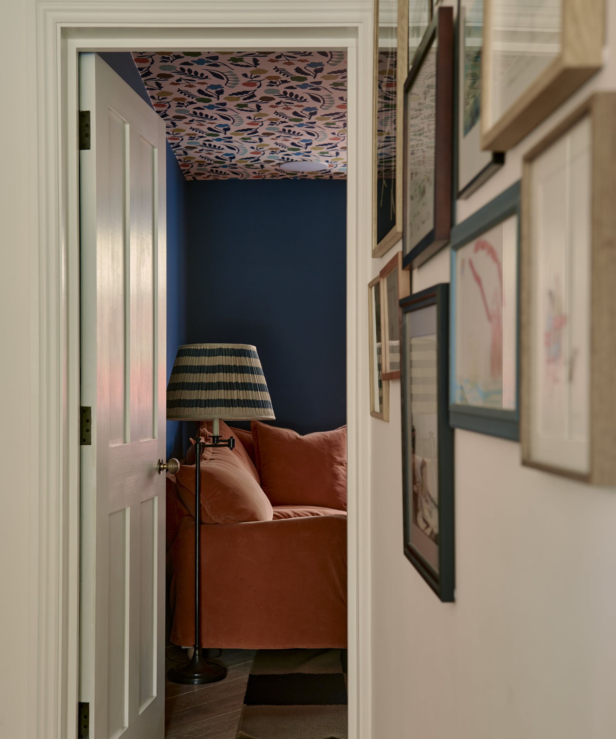 A view into a snug decorated with dark blue paint on the walls and a pink and blue patterned wallpaper on the ceiling