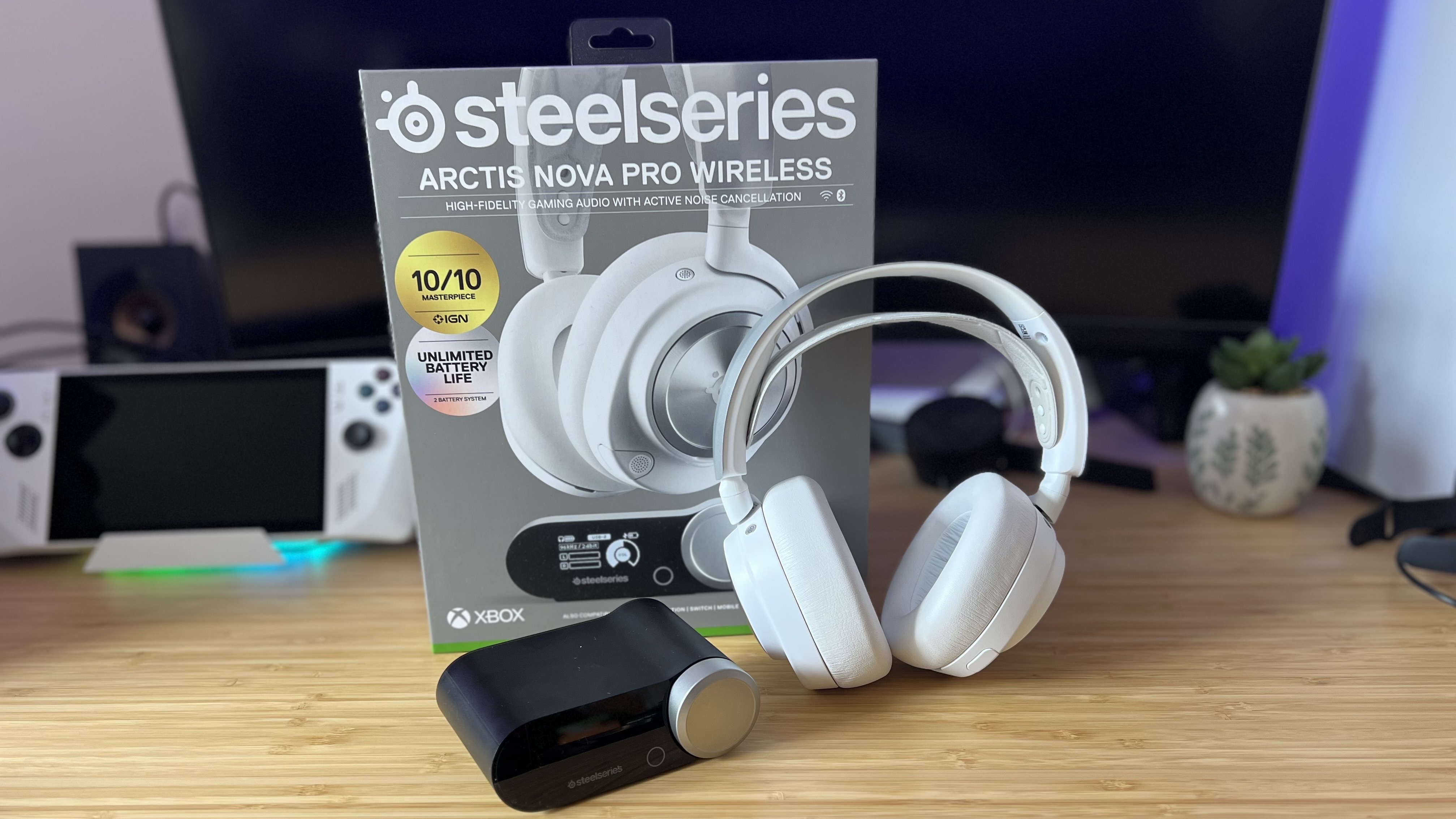 SteelSeries Arctis Nova Pro Wireless in white with packaging and hub on a wooden desk