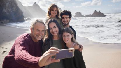 A man taking a selfie with his family on the beach. 