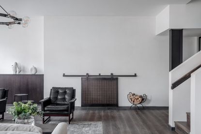 A living area with black leather chairs, a grey rug, a wooden console, a fireplace next to a staicase.