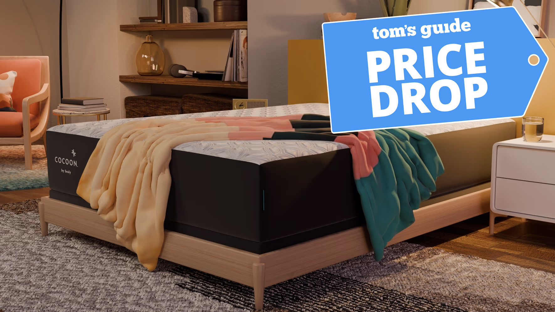 A Cocoon by Sealy Chill Hybrid Mattress on a bed frame in a bedroom, a blanket strewn on top. In the top right corner, a Tom&#039;s Guide Price Drop deals graphic