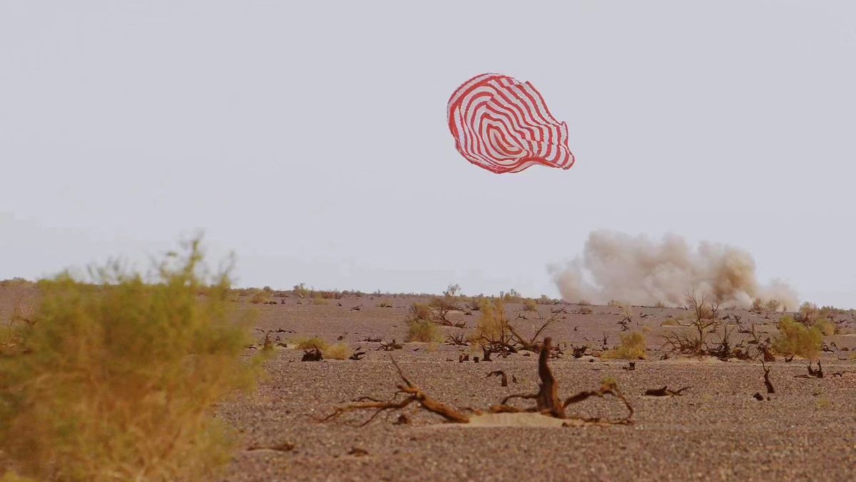 Chinese Shenzhou 15 capsule kicking up dust cloud while landing as parachute floats to Earth