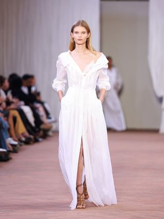 Alberta Ferretti Spring/Summer 2024 runway. Model wears a white dress and gladiator sandals.