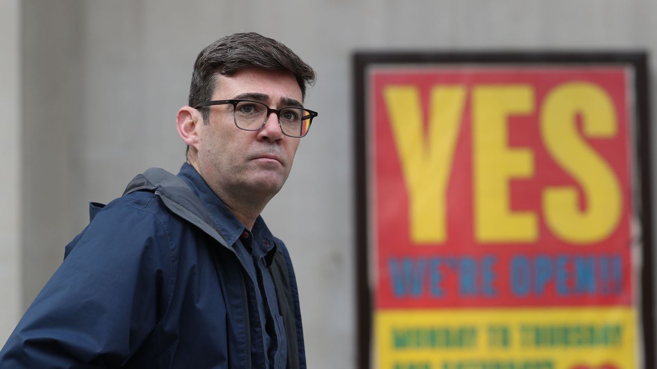 Mayor of Greater Manchester Andy Burnham stands in front of a sign advertising an open business in the city&amp;#039;s centre.