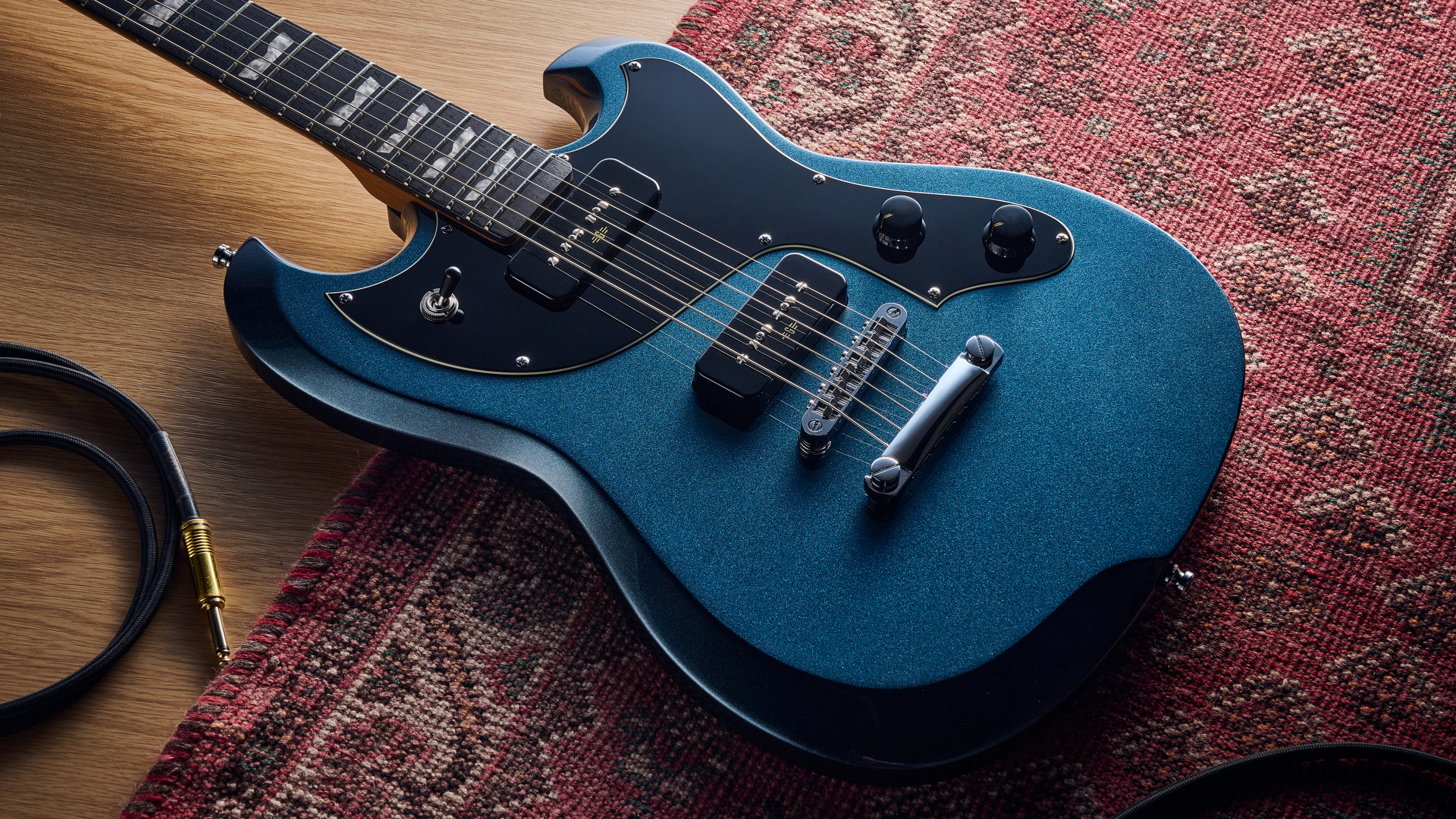 A Baum Carve electric guitar lying on a rug with a guitar cable nearby
