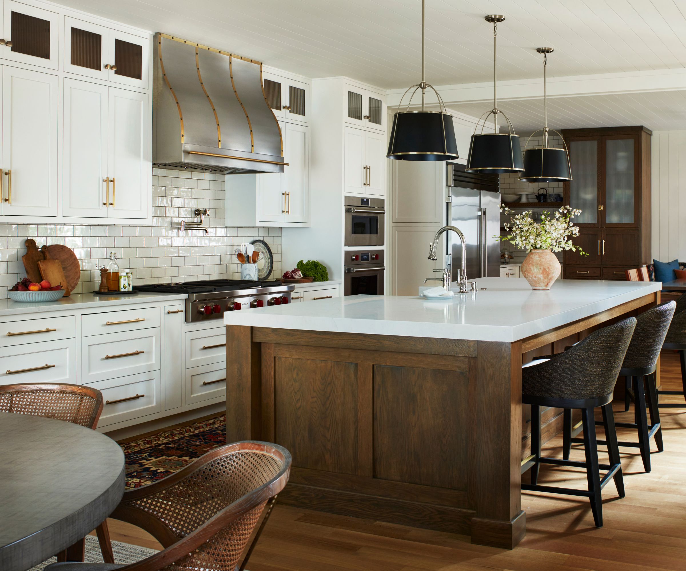 white farmhouse kitchen with wooden floors, a large wooden antique style kitchen island with black and gold pendant lights above and a statement stainless steel and copper range cooker hood