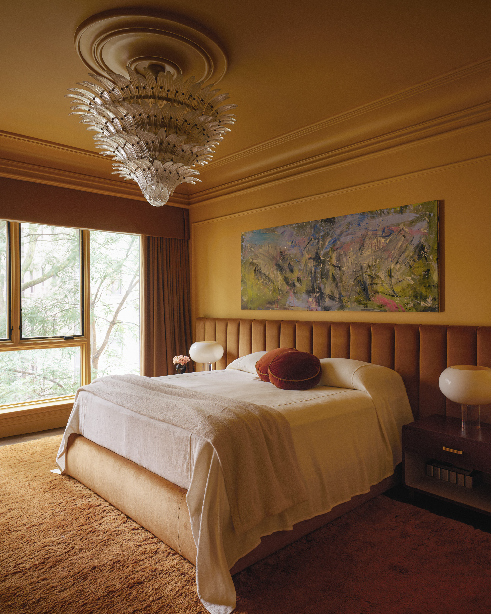 Mustard bedroom with ochre upholstered headboard, orange fluffy carpet and glass chandelier