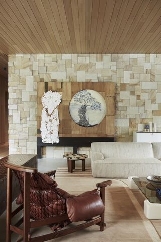 A living room with a white sofa and an accent chair that has red leather cushions and a netting on the back side of the chair. On the back wall is a sculptural art piece.