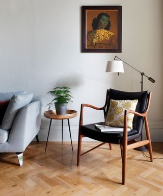 Armchair on a parquet floor with pale grey wall and sofa.