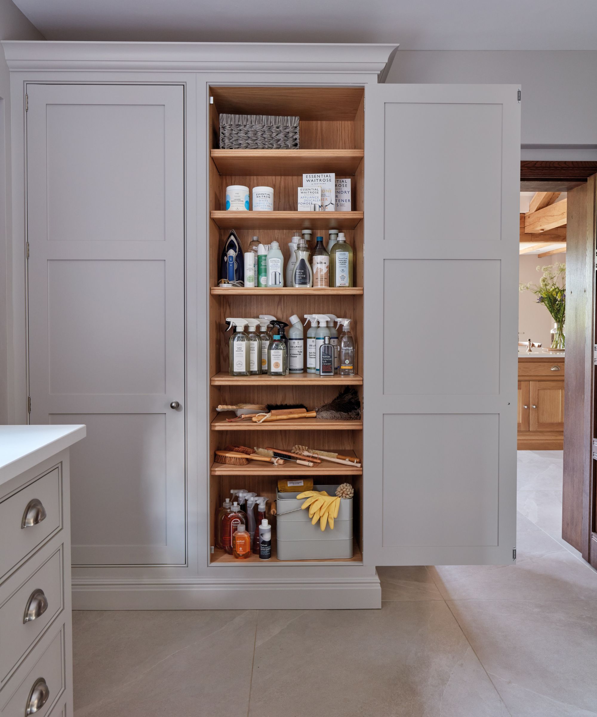 An elegant tall cupboard door opens to reveal perfectly organised shelves lined with household essentials.