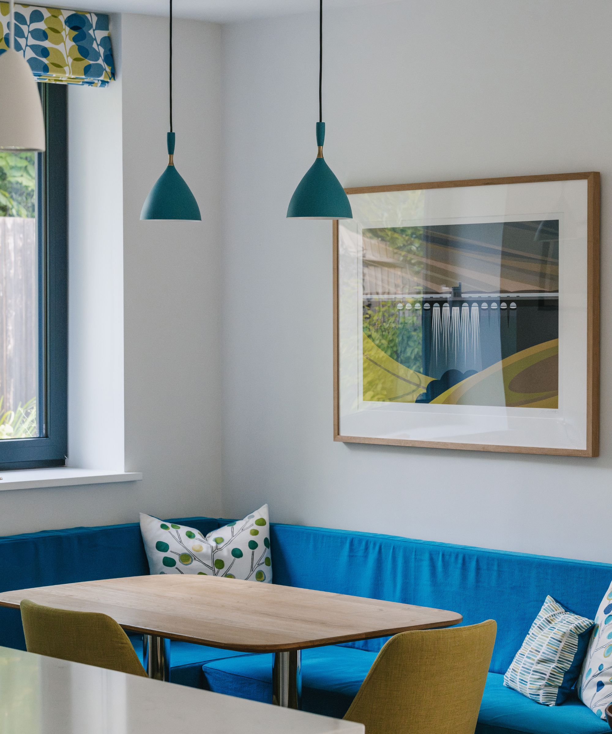Blue corner bench with wooden table opposite and two blue pendant lights hanging above